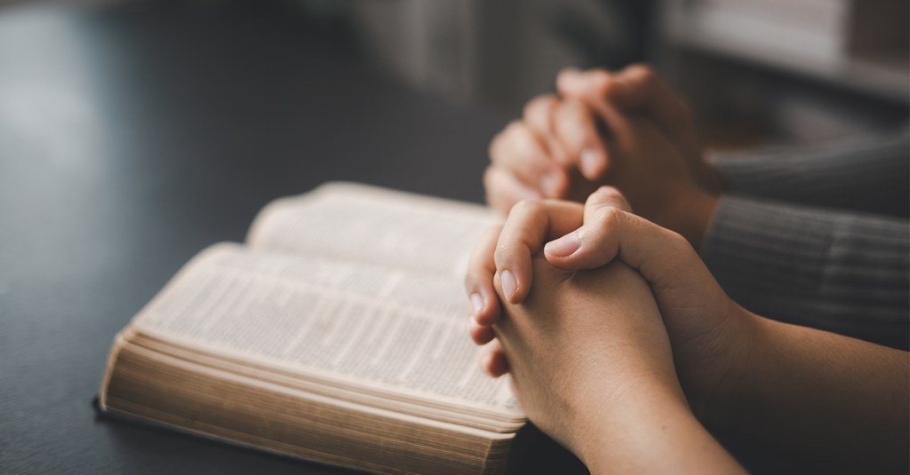 Hands folded over a Bible. Reading scripture is one suggested new year's resolutions for christians.