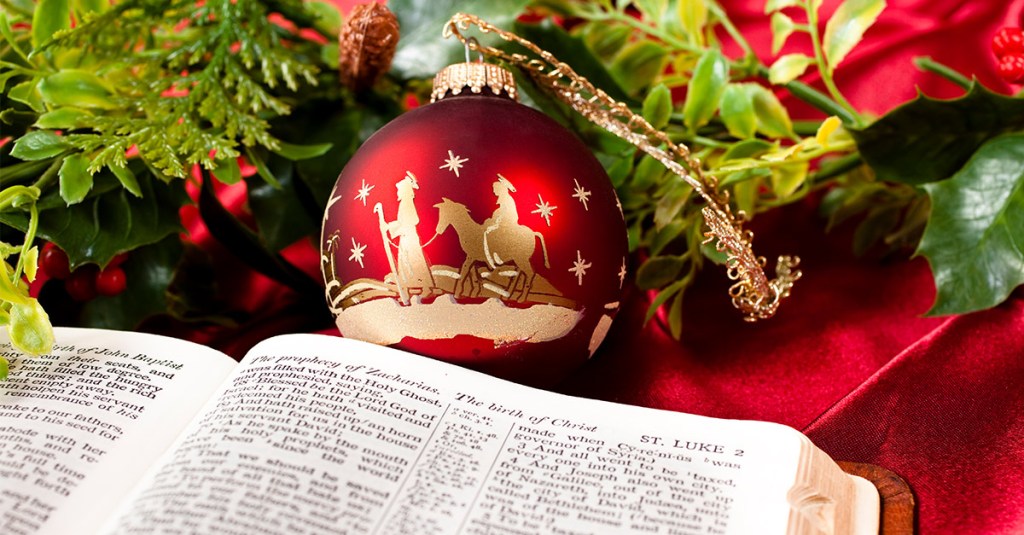 A Christmas ornament next to a tree with a Bible in the foreground