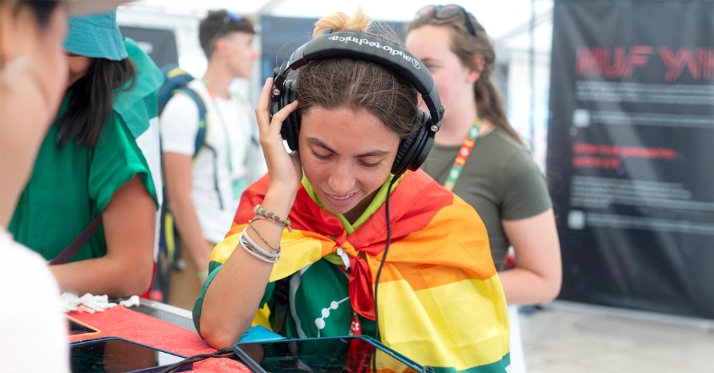 A young girl listening to heart language media on headphones. She's smiling.