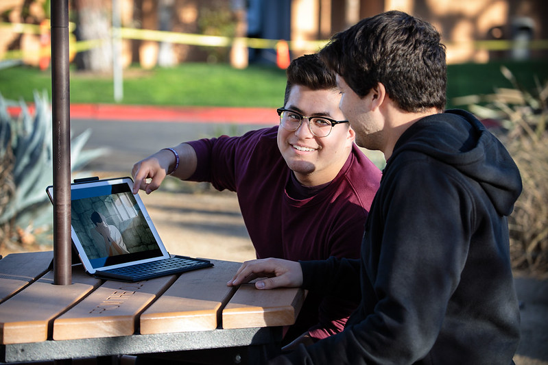 A young adult man showing another young adult man a short film on his laptop