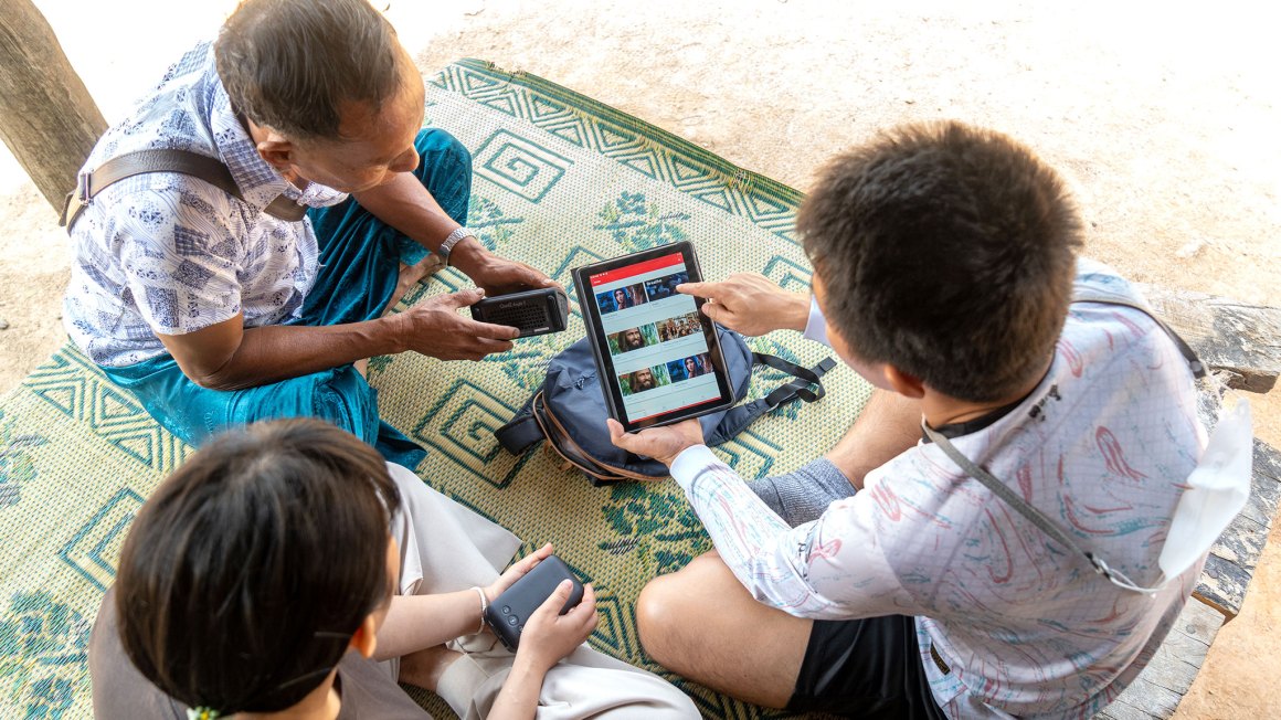 3 people sitting over a tablet with the Jesus Film App open