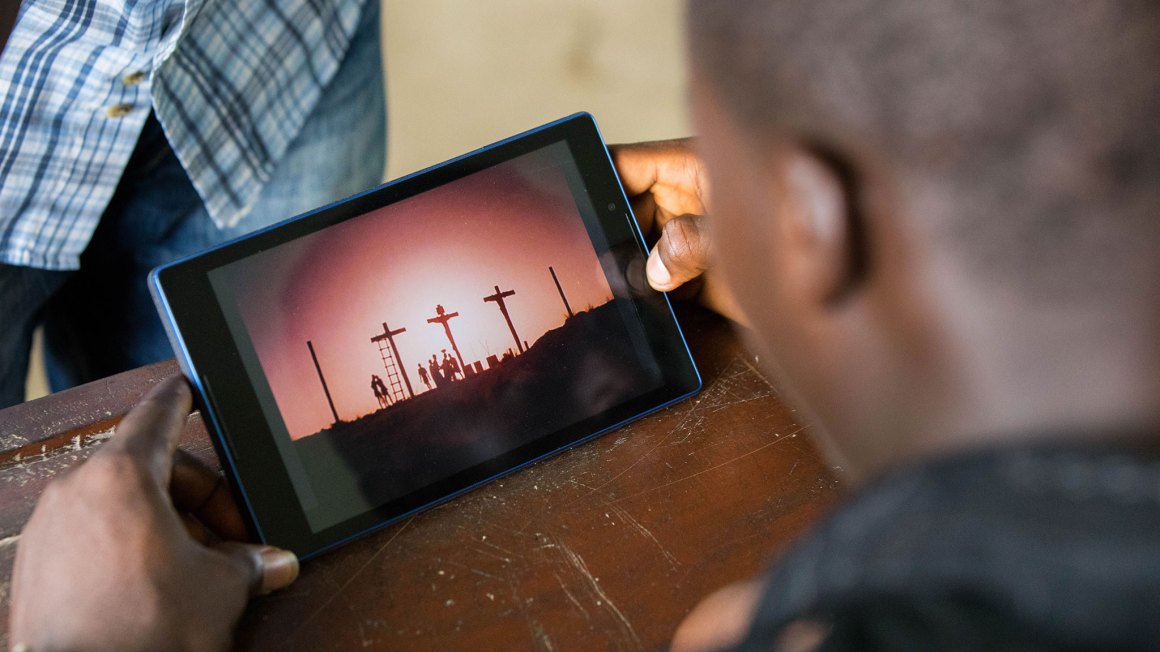 over the shoulder of a man looking at a tablet showing the Jesus Film