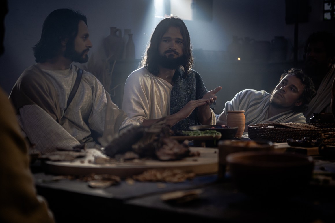 Jesus sitting at a table making the sign for forgive