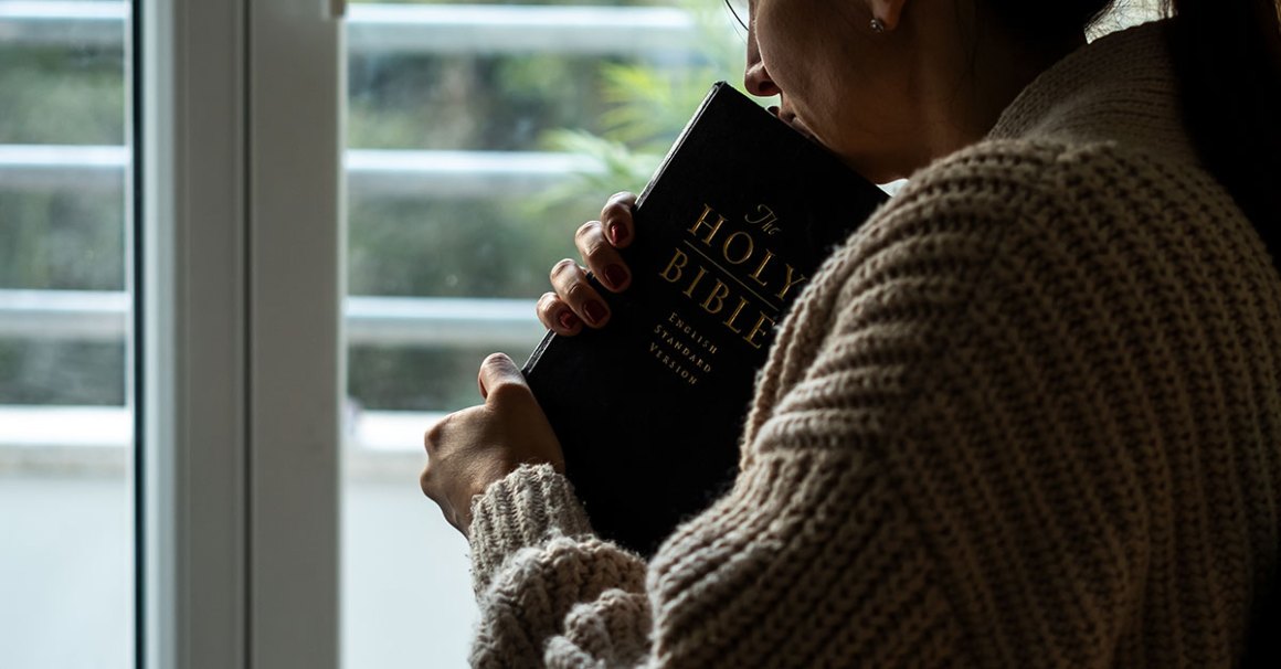 Close up of woman holding bible while looking out the window, possibly interested in evangelism scriptures