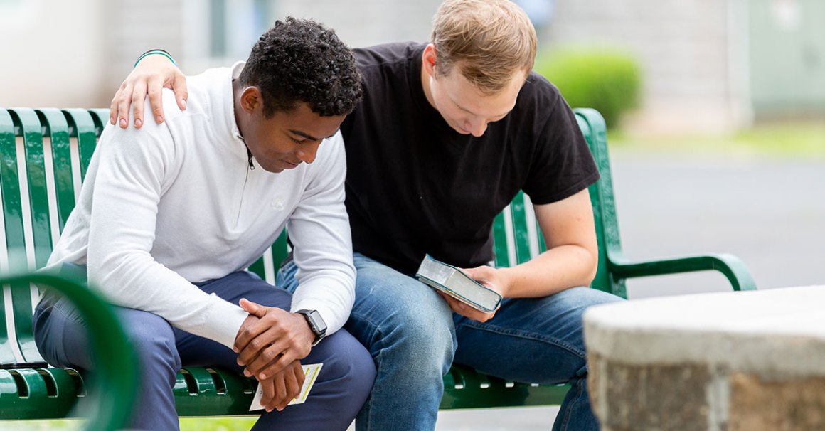 two people praying together while sitting on a bench