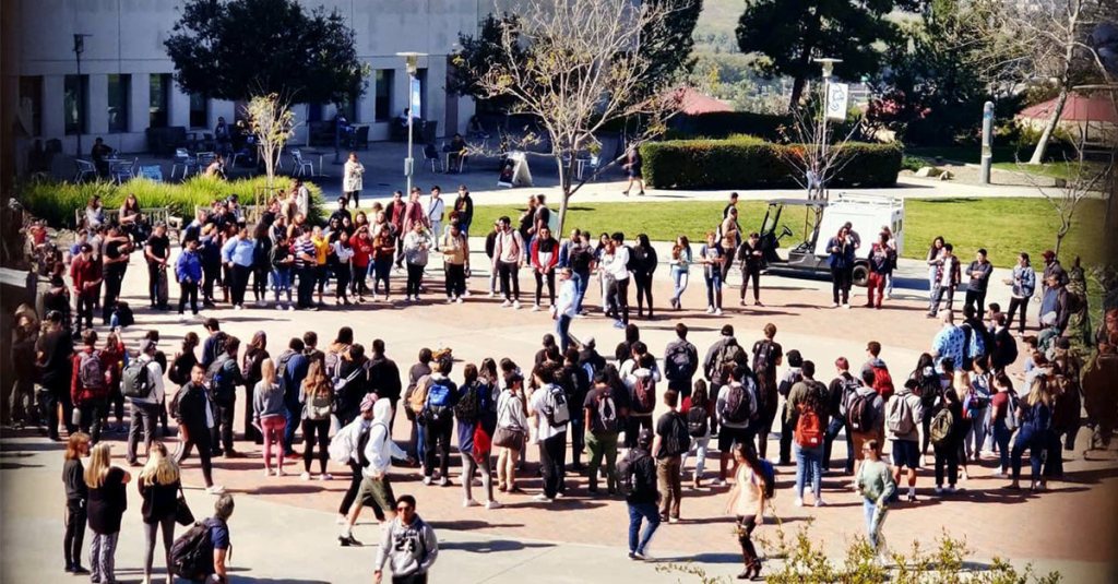 Keith Darrell is street preaching in the center of a large crowd of students on a college campus.
