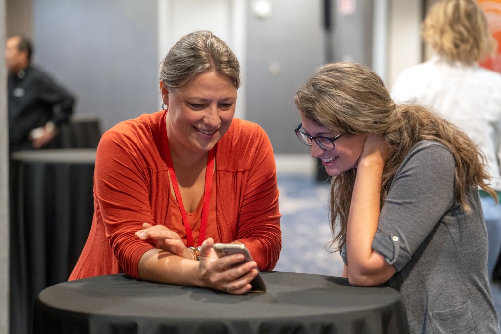One woman showing another woman a video from her phone. She's doing workplace evangelism.