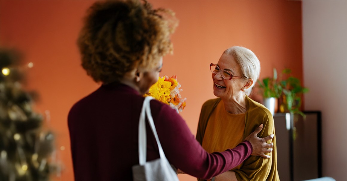Two women smiling brightly. One is handing flowers to the other. She is giving cheerfully.