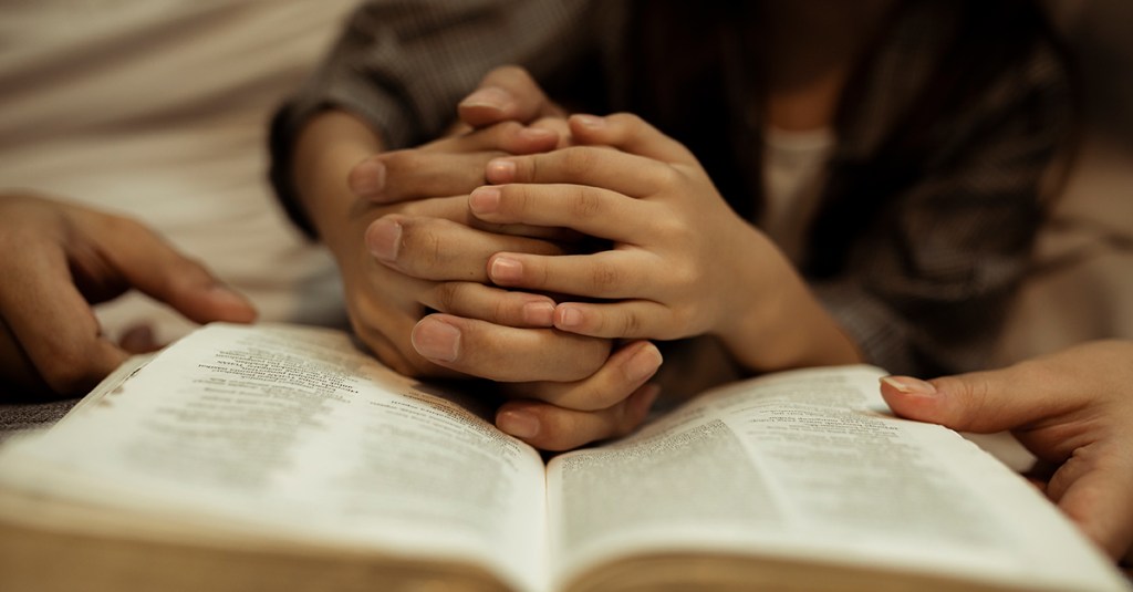 Hands folded over the bible. This post encourages Christians to keep reading the Bible